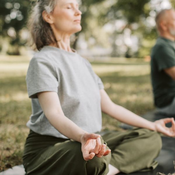 Person sitting peacefully with eyes closed in a calm, natural setting.